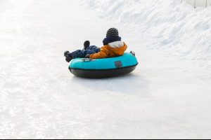 Little kid boy rolls down on ice slide on tubing. Wintertime. Fun and games, outdoor activities concept.